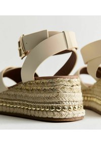 Beige espadrillo kilklackssandaler med flätad jutesula, metalliska detaljer, läderankelrem och texturerad fotbädd.