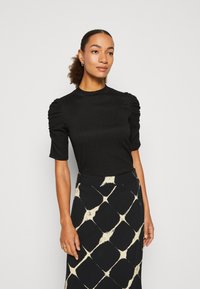 Black fitted top with short sleeves, gathered shoulders, and a high neckline, paired with a patterned high-waisted skirt in black and cream.