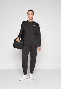 Svart sweatshirt med framficka, matchad med mörka sweatpants. Vita sneakers och en svart träningsväska finns också.