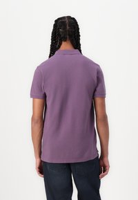 Polo cu mânecă scurtă, de culoare lavandă solidă, cu guler, textură subtilă și tiv drept, purtat cu pantaloni din denim închis.