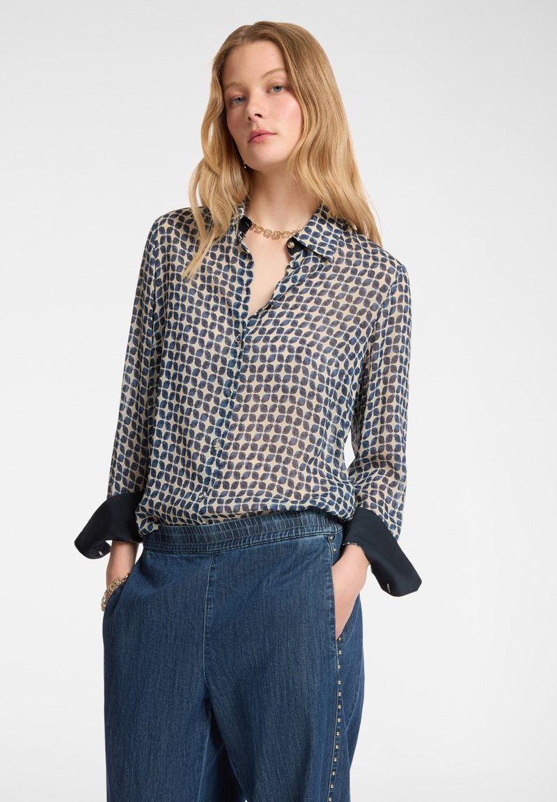 Blusa a maniche lunghe blu e crema con motivo, abbottonatura frontale e colletto blu scuro. Indossata con pantaloni di denim a vita alta.