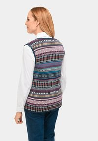 Multikleurige gebreide vest met blauwe, roze en groene strepen. Gebreide stof. Draagt over een witte lange mouwen shirt. Casual ontwerp.