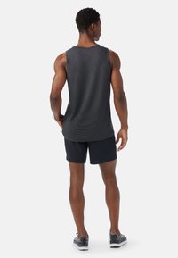 Top deportivo negro sin mangas con un patrón texturizado, combinado con pantalones cortos oscuros, visto desde atrás. Presenta un diseño ajustado y zapatillas deportivas.