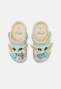 Crocs featuring a light gray base, with a green character face design, embellishments, and decorative details in various colors.