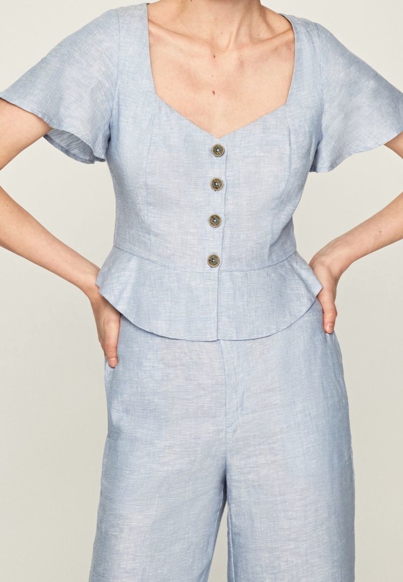 Helles blauer Peplum-Oberteil mit kurzen Ärmeln, viereckigem Ausschnitt und einer fünfknöpfigen Frontverschluss. Hergestellt aus texturiertem Stoff mit einer weichen Oberfläche.