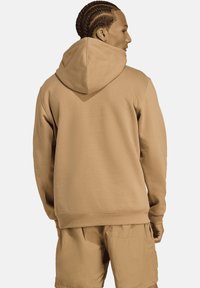 Beige hoodie gemaakt van zachte stof, met een ontspannen pasvorm, geribbelde manchetten en een grote achterzak, gecombineerd met bijpassende shorts.