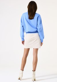 Sudadera azul clara con puños acanalados, combinada con una falda de mezclilla crema que presenta costuras verticales, y botas de tobillo blancas con acentos de tachuelas.
