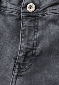 Tissu en denim gris avec des coutures visibles, une poche avant et un bouton en métal proéminent avec le texte "STREET." Détail en gros plan.