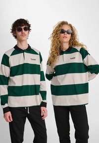 Gröna och beige randiga långärmade polo-tröjor med svart krage. Två modeller som bär mörka byxor och solglasögon. Logotyp på bröstet.