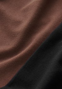 Primo piano di tessuto morbido marrone e nero con trama a maglia visibile e pieghe delicate.