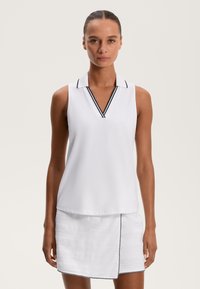 Kobieta w białej bezrękawnikowej koszulce polo w czarne paski oraz w białej spódnicy o subtelnej fakturze z czarnym wykończeniem.