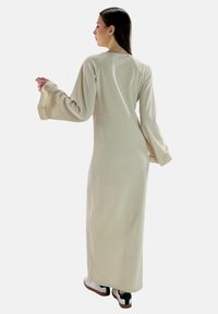 Vestido largo beige con un corte relajado, mangas acampanadas y cuello redondo. La tela parece suave, con una textura lisa y detalles mínimos.
