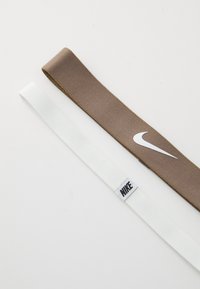 Dva trakom: jedan smeđi od tkanine s bijelim Nike logotipom; jedan bijeli s crnim Nike oznakom. Oboje su ravni i glatke teksture.