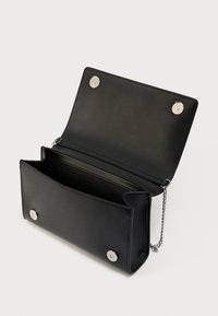 Μαύρη δερμάτινη τσάντα χειρός με ορθογώνιο σχήμα, διαθέτει εμπρός καπάκι, ασημί μεταλλικά στοιχεία, κούμπωμα με τρουκ και λουρί με αλυσίδα. Στο εσωτερικό υπάρχει μία κύρια θήκη.