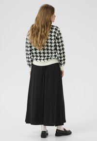 Black and white houndstooth knit sweater with a loose fit, paired with a flowing black maxi skirt and black loafers. Smooth texture.