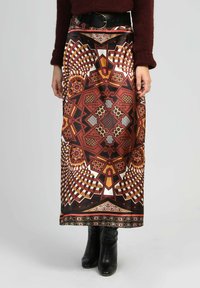 Jupe taille haute avec un motif géométrique symétrique en marron, orange, noir et blanc, associée à des bottines noires et un pull bordeaux.