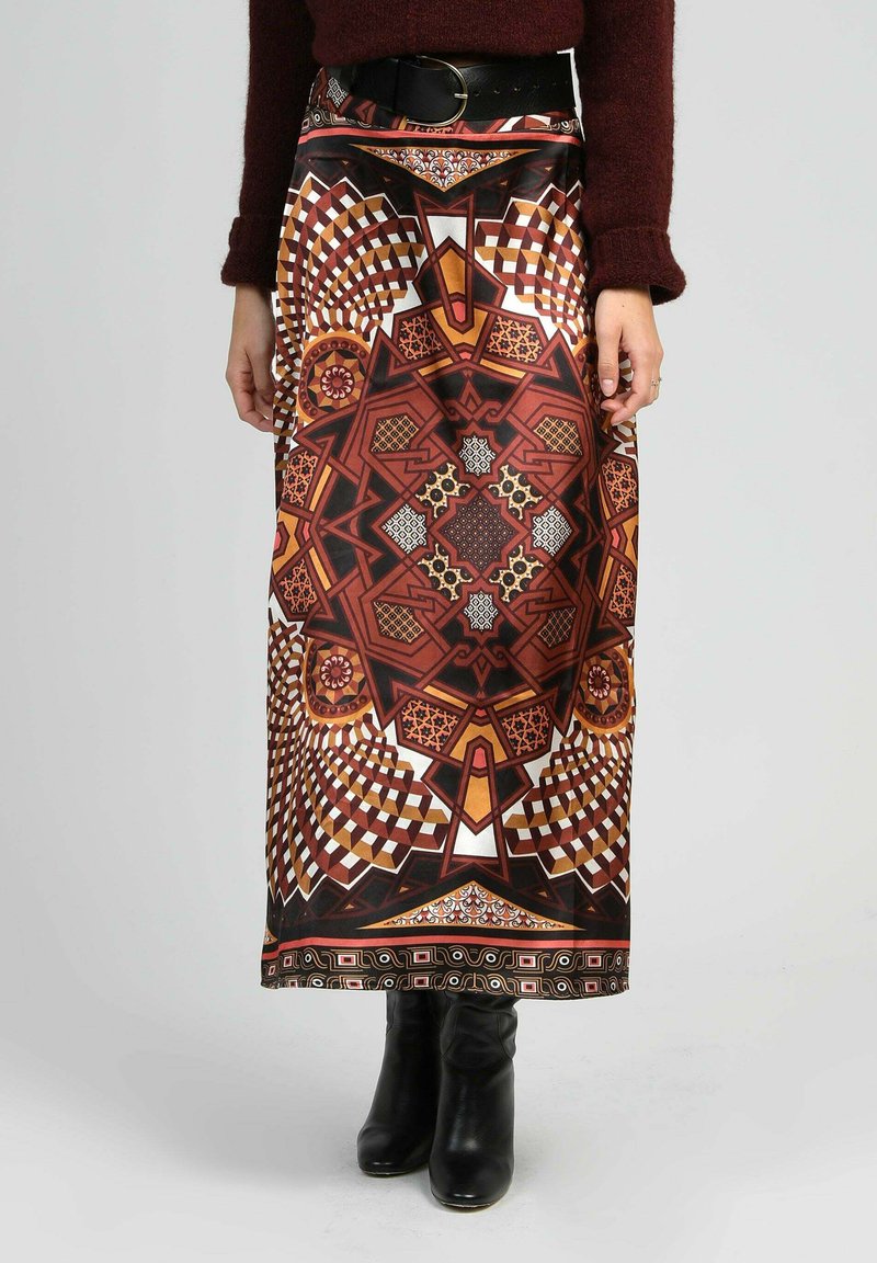 Jupe taille haute avec un motif géométrique symétrique en marron, orange, noir et blanc, associée à des bottines noires et un pull bordeaux.