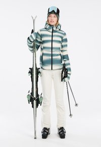 Skiausrüstung mit einer türkis-weißen gestreiften Daunenjacke, weißen Hosen, schwarzen Skistiefeln und Skistöcken, die passende Skier mit grünen Akzenten hält.