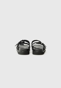Black sandals with a wide strap design and adjustable buckle closure. Features a cushioned footbed and textured sole for grip.
