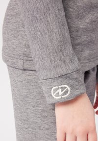 Maglietta grigia a maniche lunghe realizzata in un tessuto morbido e testurizzato. Presenta un logo bianco sul polsino, che mette in risalto un design semplice e rilassato.