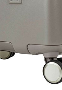 Maleta rígida de color gris claro con acabado texturizado. Cuenta con cuatro ruedas de diseño bicolor, bordes redondeados y un área de asa empotrada.