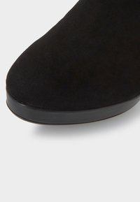 Botín de ante negro con punta redondeada y suela de goma negra lisa. La superficie tiene una textura suave con un detalle mínimo.