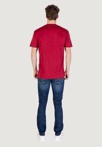 T-shirt di cotone color marsala con colletto a giroclassico, abbinato a jeans in denim blu. Tessuto morbido, design semplice, senza motivi visibili.