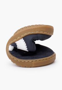Scarpe per bambini con un design flessibile, parte superiore blu scuro, dettagli in pelle bianca, interno morbido e suola in gomma marrone testurizzata.