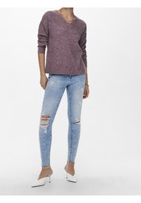Jasnofioletowy sweter dzianinowy z dekoltem w serek, połączony z przetartymi jasnoniebieskimi skinny jeansami z dziurami. Uzupełniony białymi szpilkami w szpic.