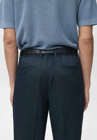 Spodnie w kolorze granatowym o dopasowanym kroju, z gładkim przodem, kieszeniami bocznymi i dwoma guzikami z tyłu, zestawione z jasnoniebieskim swetrem z dzianiny.