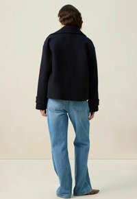 Veste en mélange de laine bleu marine avec une silhouette épurée, un large col et des manches retroussées, assortie à un jean droit bleu clair.