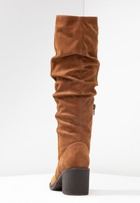 Brown leather thigh-high boot with gathered texture, round toe, and chunky heel. Features a side zipper for easy wear.