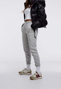 Szare bawełniane spodnie dresowe ze ściągaczami przy kostkach, zestawione z czarną pikowaną kurtką. Na nogach zielono-beżowe buty sportowe oraz białe skarpetki.