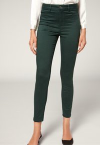 Pantalones vaqueros ajustados de color verde oscuro con una textura suave, de cintura alta y diseño de cinco bolsillos. Cuenta con un cierre frontal de botón y cremallera.