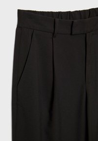 Pantalon noir avec un design plissé, une ceinture élastique et des poches latérales. Confectionné dans un tissu lisse et doux.