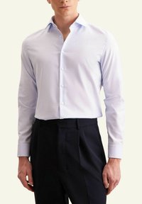 Camicia azzurra chiara con maniche lunghe, colletto a punta e una superficie liscia, abbinata a pantaloni scuri.