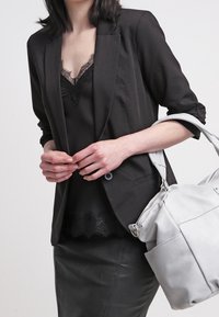 Svart kavaj över en svart topp med spetsdetaljer, kombinerat med en svart läderkjol. Håller en grå handväska med silverdetaljer och justerbar rem.