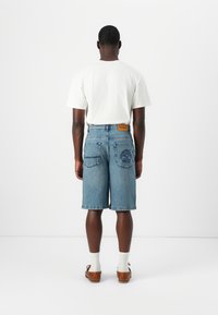 Hellblaue Jeansshorts, lockere Passform, knielang, mit zwei Rücken Taschen. Weißes Baumwoll-T-Shirt, braune Lederschuhe und weiße Socken.