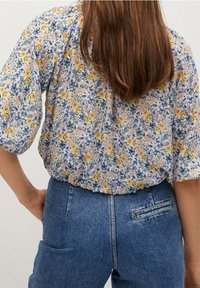 Blouse fleurie avec motifs roses, jaunes et bleus ; manches courtes amples ; tissu léger ; associée à un jean en denim bleu taille haute.