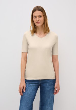 Haut beige à manches courtes et décolleté en V, fabriqué dans un tissu doux et lisse. Conçu avec une silhouette ajustée et un aspect épuré et minimaliste.