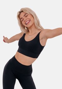 Black sports bra with a scoop neckline, wide straps, and a banded bottom. Smooth, stretchy fabric with a seamless design. Paired with black leggings.