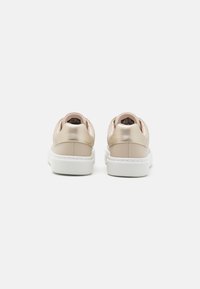 Adidași din piele bej cu accente metalice, toc rotund, călcâi căptușit și talpă din cauciuc alb. Textură netedă cu caracteristici de design minime.