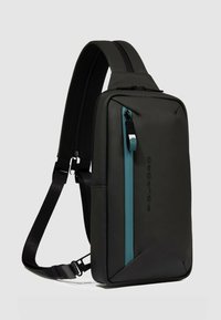 Zwarte schoudertas met een gladde matte afwerking, voorzien van een turquoise ritssluiting en verstelbare band. Rechthoekige vorm met een minimalistisch ontwerp.