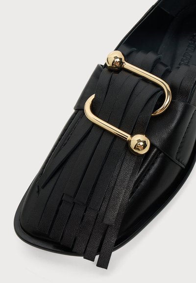 Mocassin en cuir noir avec des franges et une barre métallique incurvée dorée avec des extrémités sphériques sur le dessus avant.