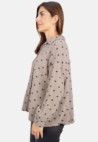 Langärmliges, beige Hemd aus strukturiertem Stoff mit einem Muster aus kleinen schwarzen Herzen und einem Kragen.