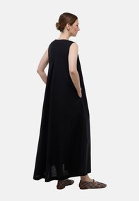 Robe maxi sans manches noire avec une coupe décontractée, dotée de poches latérales et d'un léger pli au dos. Associée à des chaussures à enfiler à motifs.