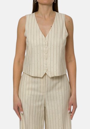 Donna che indossa un gilet beige senza maniche a righe sottili con pantaloni a vita alta abbinati su uno sfondo semplice.