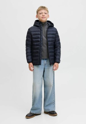 Padded navyblauer Mantel mit Kapuze, kombiniert mit einem grauen Rollkragenoberteil, weiten hellblauen Jeans und Schuhen mit brauner Sohle. Glatter Stoff, lässige Passform.
