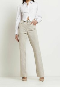 Camisa blanca, recortada, de botones y de manga larga con bolsillos frontales, combinada con unos vaqueros de tiro alto, beige claro y acampanados, y tacones nude.