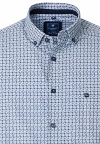 Koszula zapinana na guziki w jasnoniebieskim materiale z geometycznym wzorem. Posiada kołnierz rozpostarty oraz ciemnoniebieskie guziki z haftem logo.